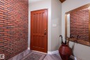 Entryway featuring a paneled wood door, wood-finish flooring, and a decorative brick accent wall - 14514 101 Avenue Nw, Edmonton, AB 
