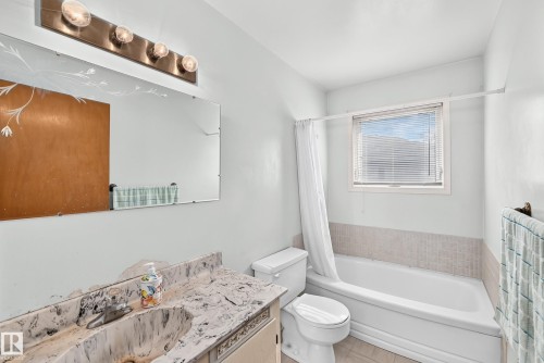 Bathroom featuring a bathtub with a shower combination, a window with horizontal blinds, and a vanity with a counter and an integrated sink - 15703 84 Avenue Nw, Edmonton, AB - Indoor Photo Showing Bathroom
