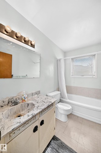 Bathroom with a single vanity featuring a stone-finish countertop and integrated sink, light-colored cabinet doors, a full-width mirror, and overhead lighting - 15703 84 Avenue Nw, Edmonton, AB - Indoor Photo Showing Bathroom