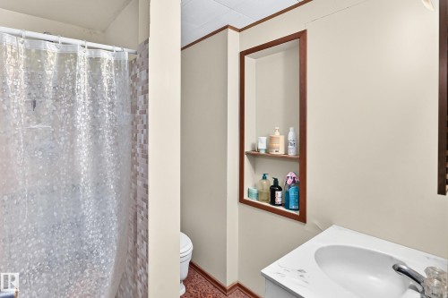 Bathroom featuring a shower with mosaic tile surround, built-in wall niche with wood trim, and a vanity with a white countertop and integrated sink - 15703 84 Avenue Nw, Edmonton, AB - Indoor Photo Showing Bathroom