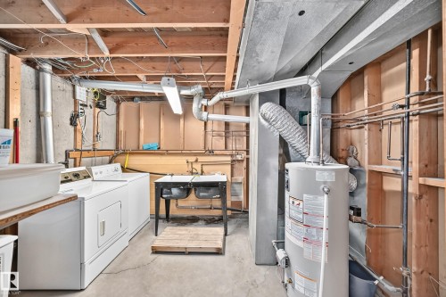 Utility room featuring exposed ceiling joists, concrete foundation walls, a double utility sink, and a water heater - 15703 84 Avenue Nw, Edmonton, AB - Indoor