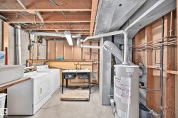 Utility room featuring exposed ceiling joists, concrete foundation walls, a double utility sink, and a water heater - 
