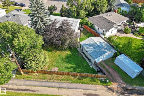 Expansive grassy lawn with established trees, featuring a detached garage, wood fencing, and a gravel driveway - 15703 84 Avenue Nw, Edmonton, AB - Outdoor