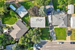 Aerial view showcasing a residential property with a shingled roof, a green lawn, and a paved driveway - 