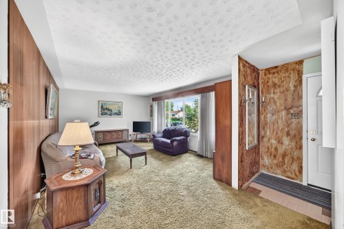 Living area featuring wood-paneled walls, textured ceiling, a large window, and green carpeting - 15703 84 Avenue Nw, Edmonton, AB - Indoor Photo Showing Other Room