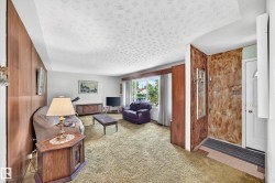 Living area featuring wood-paneled walls, textured ceiling, a large window, and green carpeting - 