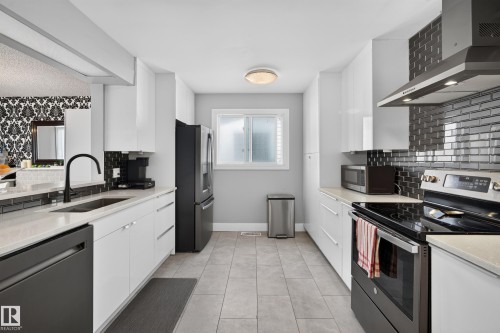 Galley kitchen featuring white cabinetry, light-toned countertops, black subway tile backsplash, and stainless steel appliances - 13512 111 Street Nw, Edmonton, AB 