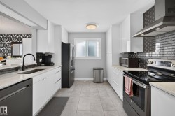 Galley kitchen featuring white cabinetry, light-toned countertops, black subway tile backsplash, and stainless steel appliances - 