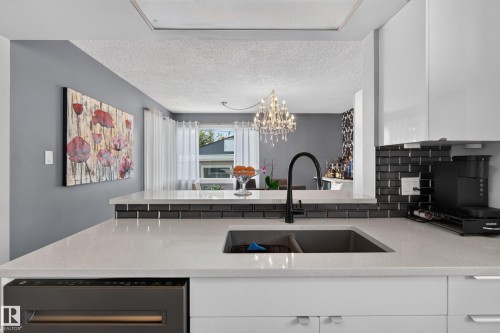 White countertop with an undermount sink and matte black faucet, dark subway tile backsplash, white upper and lower cabinetry, and a built-in dishwasher - 13512 111 Street Nw, Edmonton, AB 