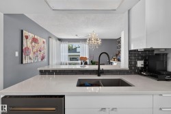 White countertop with an undermount sink and matte black faucet, dark subway tile backsplash, white upper and lower cabinetry, and a built-in dishwasher - 