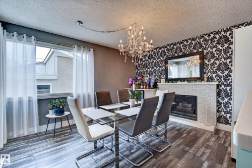 Dining area with wood-finish flooring, a crystal chandelier, and a decorative fireplace with a mantel - 13512 111 Street Nw, Edmonton, AB 