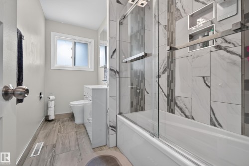 Wood-finish tile flooring, white vanity with integrated sink, white bathtub with a glass shower enclosure, and tiled shower walls with recessed niches - 13512 111 Street Nw, Edmonton, AB 