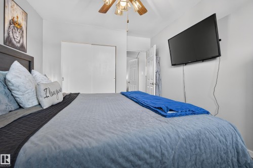 Ceiling fan with light fixture, sliding closet doors, wood-finish headboard, wall-mounted television, and a white paneled door - 13512 111 Street Nw, Edmonton, AB 