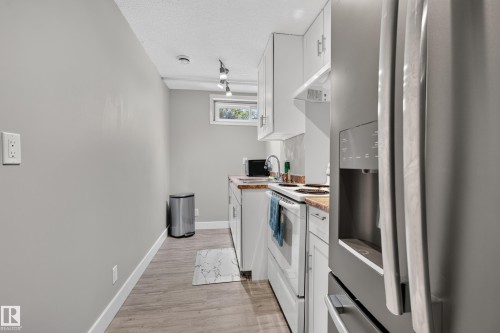 Kitchenette featuring white cabinetry, light wood-finish countertops, stainless steel refrigerator, and wood-finish flooring - 13512 111 Street Nw, Edmonton, AB 