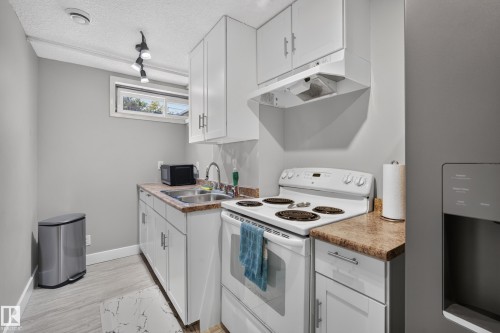 Kitchenette featuring white cabinetry, a double basin sink, a white electric range, and light-toned countertops - 13512 111 Street Nw, Edmonton, AB 