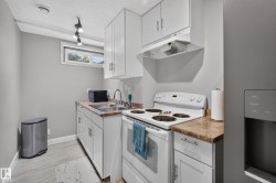 Kitchenette featuring white cabinetry, a double basin sink, a white electric range, and light-toned countertops - 