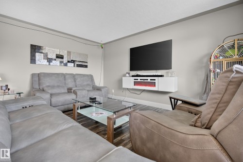 Wood-finish flooring, light gray walls, white ceiling, and a wall-mounted media console with an integrated electric fireplace - 13512 111 Street Nw, Edmonton, AB 