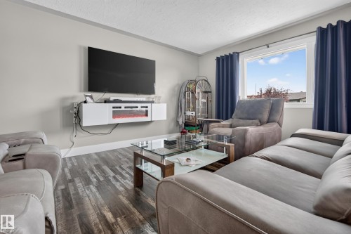 Wood-finish flooring with a wall-mounted media console featuring an integrated electric fireplace - 13512 111 Street Nw, Edmonton, AB 