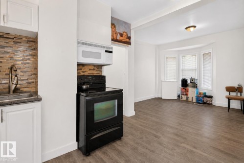 Functional kitchen space featuring white cabinetry, a stainless steel sink, and a multi-toned tile backsplash - 9124 119 Avenue Nw, Edmonton, AB - Indoor