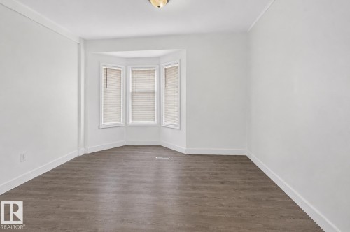 Room featuring a bay window with blinds, wood-finish flooring, white walls, white baseboards, and crown molding - 9124 119 Avenue Nw, Edmonton, AB - Indoor Photo Showing Other Room