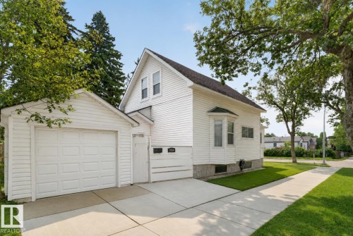 White siding exterior featuring a detached garage with a paneled door, a concrete driveway, a bay window, and a sidewalk - 9124 119 Avenue Nw, Edmonton, AB - Outdoor