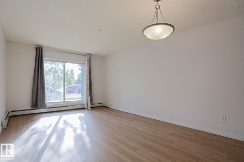 Wood-finish flooring, white walls, large window, and a built-in ceiling light fixture - #108 1204 156 St Nw, Edmonton, AB 