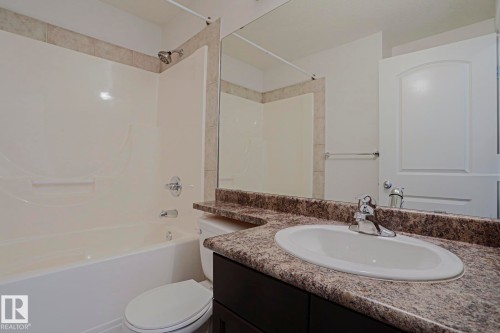 Built-in bathtub with shower, tiled surround, vanity with an integrated sink, and a large wall mirror - #108 1204 156 St Nw, Edmonton, AB 