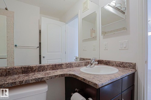 Bathroom featuring a vanity with an integrated sink, dark wood-finish cabinetry, speckled countertop, and a wall-mounted mirror - #108 1204 156 St Nw, Edmonton, AB 