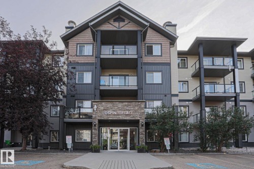 Multi-story residential building featuring balconies with glass railings, a stone facade entrance, and varied siding materials - #108 1204 156 St Nw, Edmonton, AB 