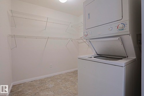Dedicated utility space featuring a stacked washer and dryer, tile flooring, and multiple wire shelving units - #108 1204 156 St Nw, Edmonton, AB 