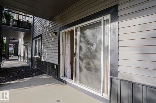 Patio with a concrete surface, featuring a sliding glass door, horizontal siding, and a wall-mounted light fixture - #108 1204 156 St Nw, Edmonton, AB 