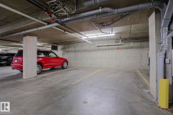 Concrete flooring in a subterranean parking area, featuring exposed overhead piping and fluorescent lighting fixtures - 