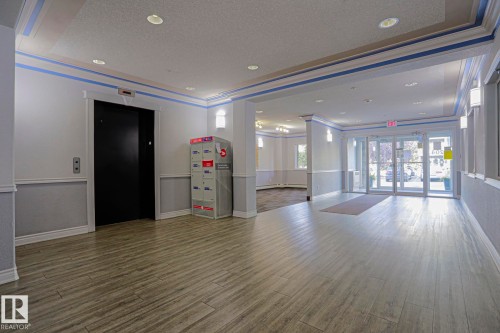 Lobby area featuring wood-finish flooring, recessed lighting, wall sconces, and a black elevator door - #108 1204 156 St Nw, Edmonton, AB 