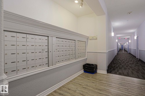 Wall-mounted mailboxes set within a decorative frame, track lighting, two-tone wall treatment, wood-finish flooring, and patterned carpet - #108 1204 156 St Nw, Edmonton, AB 