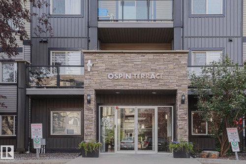 Stone-clad entrance with glass double doors, featuring integrated exterior lighting and a building nameplate - #108 1204 156 St Nw, Edmonton, AB 