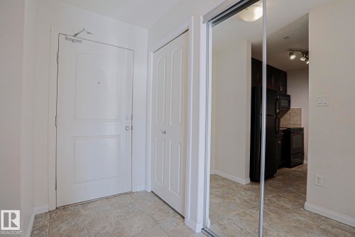 Tiled flooring, white paneled door, built-in mirrored closet, track lighting, and dark wood-finish cabinetry - #108 1204 156 St Nw, Edmonton, AB 