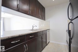Kitchen featuring dark wood-finish cabinetry, light-colored countertops, dual basin stainless steel sink, and tile backsplash - 