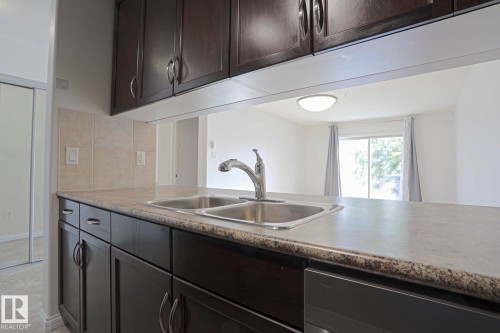 Kitchen featuring dark wood cabinetry, a double basin stainless steel sink, and a light-toned countertop - #108 1204 156 St Nw, Edmonton, AB 