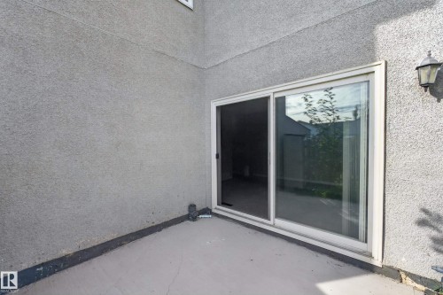 Concrete patio with a stucco exterior, featuring a sliding glass door and an exterior wall lantern - 17749 95 Street Nw, Edmonton, AB 