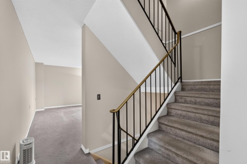 Carpeted staircase with black metal balusters and a brass handrail - 17749 95 Street Nw, Edmonton, AB 