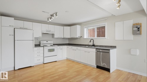 Kitchen featuring wood-finish flooring, white cabinetry, integrated range with overhead hood, and a stainless steel dishwasher - 12208 146 Avenue Nw, Edmonton, AB 