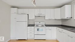 Kitchen featuring white cabinetry, dark speckled countertops, white appliances, track lighting, and wood-finish flooring - 