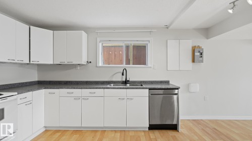 White cabinetry with brushed nickel hardware, dark speckled countertops, stainless steel dishwasher, black gooseneck faucet, and wood-finish flooring - 12208 146 Avenue Nw, Edmonton, AB 