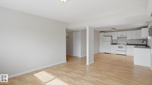 Light wood-finish flooring throughout, white kitchen cabinetry, white appliances, dark countertops, and a black gooseneck faucet - 12208 146 Avenue Nw, Edmonton, AB 