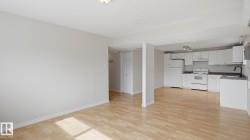 Light wood-finish flooring throughout, white kitchen cabinetry, white appliances, dark countertops, and a black gooseneck faucet - 