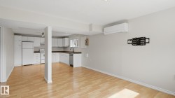 Open-concept living space featuring wood-finish flooring, white cabinetry, a built-in dishwasher, and an installed wall-mounted air conditioning unit - 