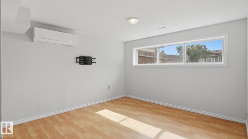 Wood-finish flooring with white baseboards, a horizontal window, and a wall-mounted mini-split system - 12208 146 Avenue Nw, Edmonton, AB 