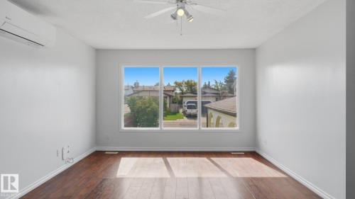 Expansive room featuring rich wood-finish flooring, a wall-mounted mini-split air conditioning unit, and a ceiling fan with integrated lighting - 12208 146 Avenue Nw, Edmonton, AB 