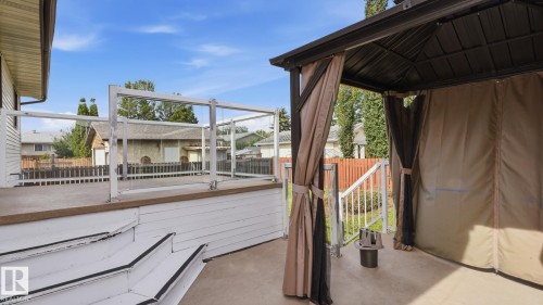 Outdoor deck featuring glass panel railing, white wood stairs, and an attached gazebo with privacy curtains - 12208 146 Avenue Nw, Edmonton, AB 