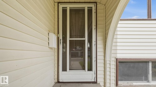 Exterior featuring horizontal siding, a storm door with vertical glass panels, and an arched architectural detail - 12208 146 Avenue Nw, Edmonton, AB 
